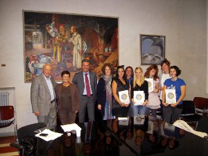 Foto di gruppo della cerimonia di consegna borse di studio Camprini Malmerendi 2009/2010, presso la Sala Nera del Comune di Cesena, alla presenza di Francesco Malmerendi (figlio di Giannetto), il Sindaco di Cesena Paolo Lucchi, l'Assessore del Comune di Cesena Simona Benedetti, la Presidente ASP Elide Urbini e gli studenti premiati. Sullo sfondo il dipinto "Mario Morigi e Malmerendi nella fabbrica di ceramiche" del 1933